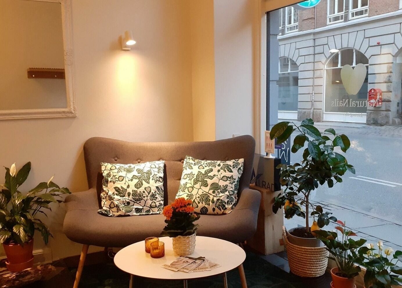 Indbydende loungeområde hos Natural Nails i København, DK, med sofa, planter og hyggelig belysning.