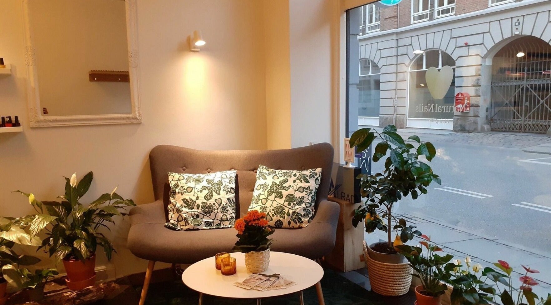 Indbydende loungeområde hos Natural Nails i København, DK, med sofa, planter og hyggelig belysning.