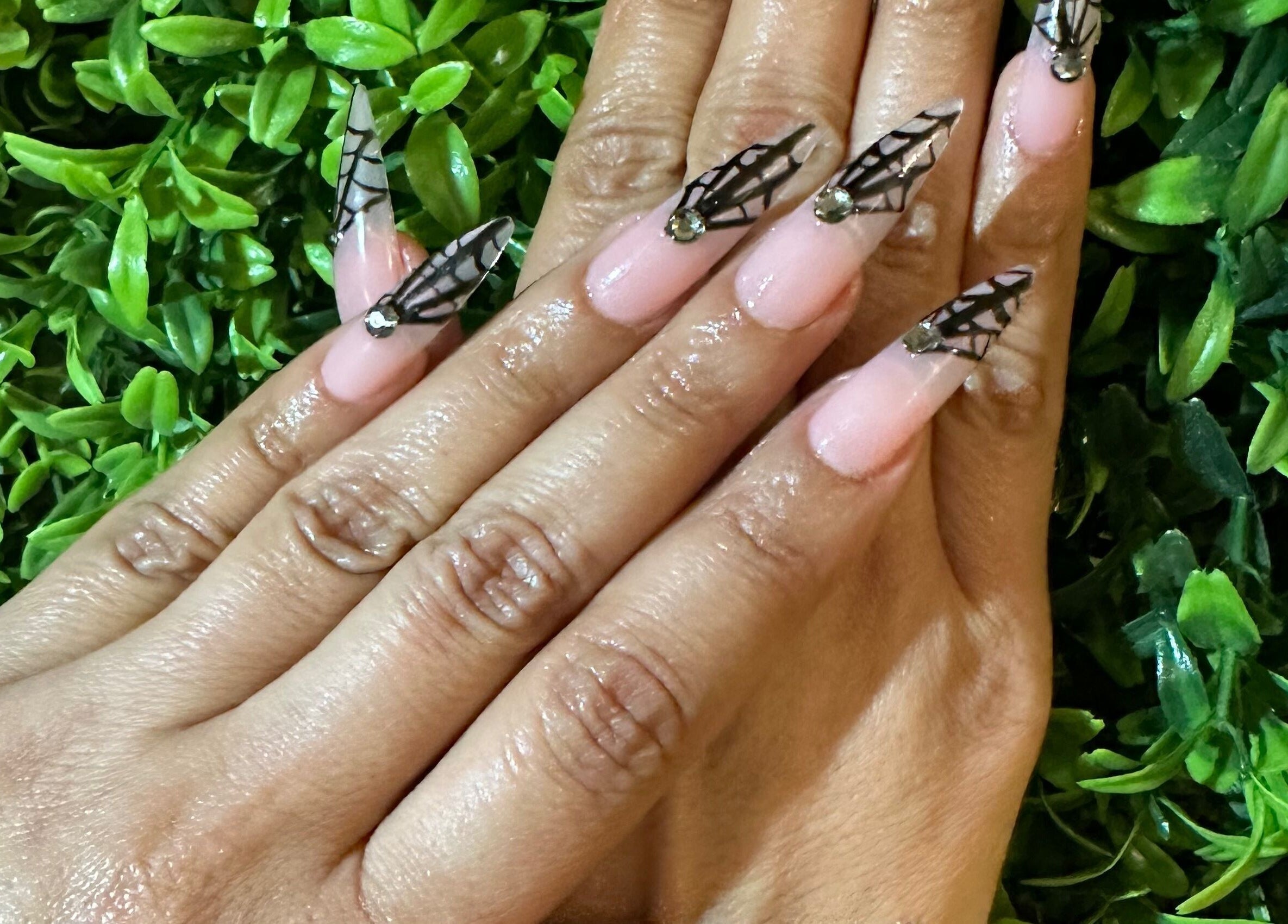 Intricate nail art on manicured hands at Lovely Me Nail Studio, Laredo, Texas, US against a green leafy backdrop.