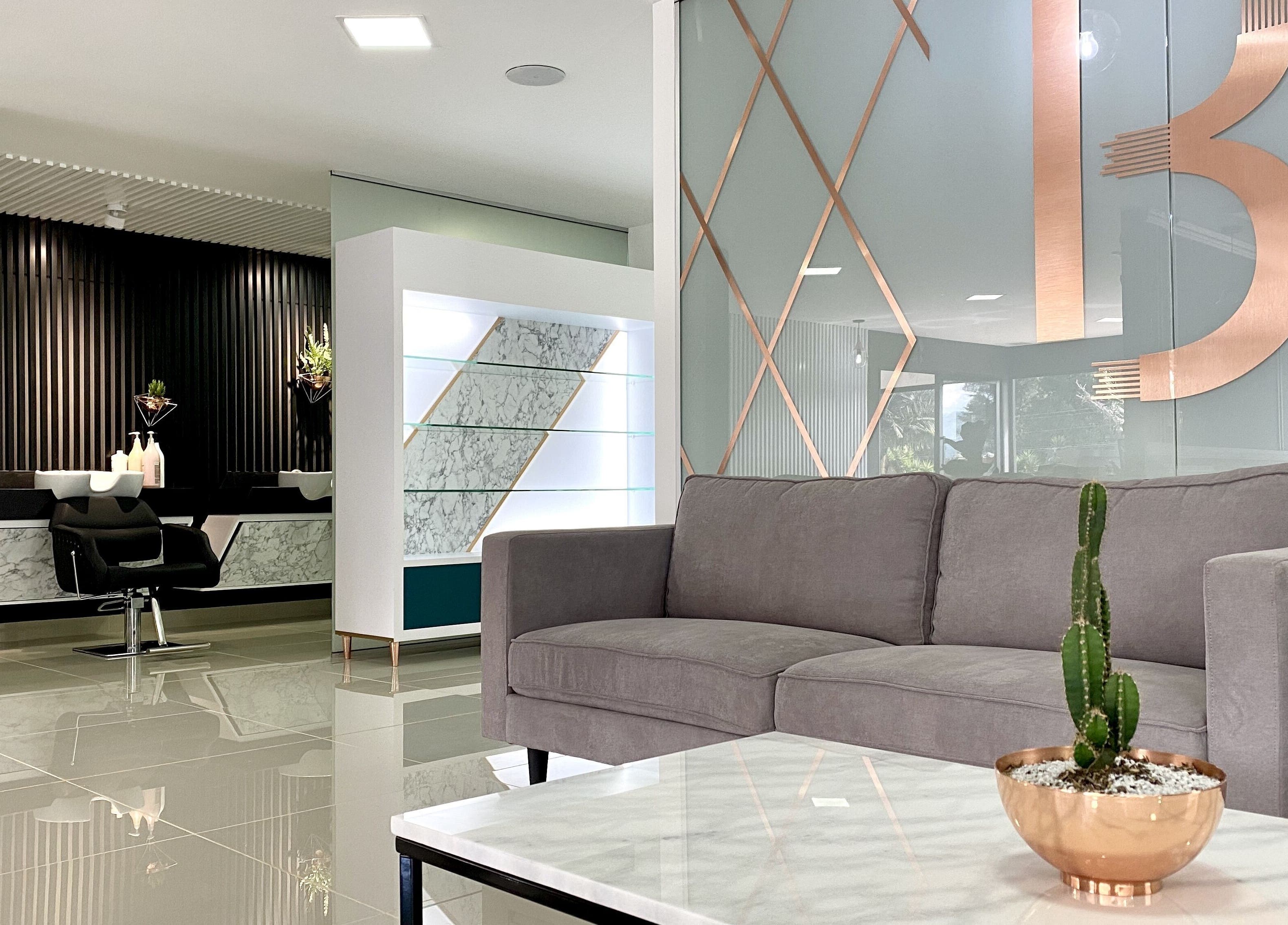 Elegante salón de B-Stetic en Rionegro, Antioquia, CO, con sofá gris, planta y espejo artístico.