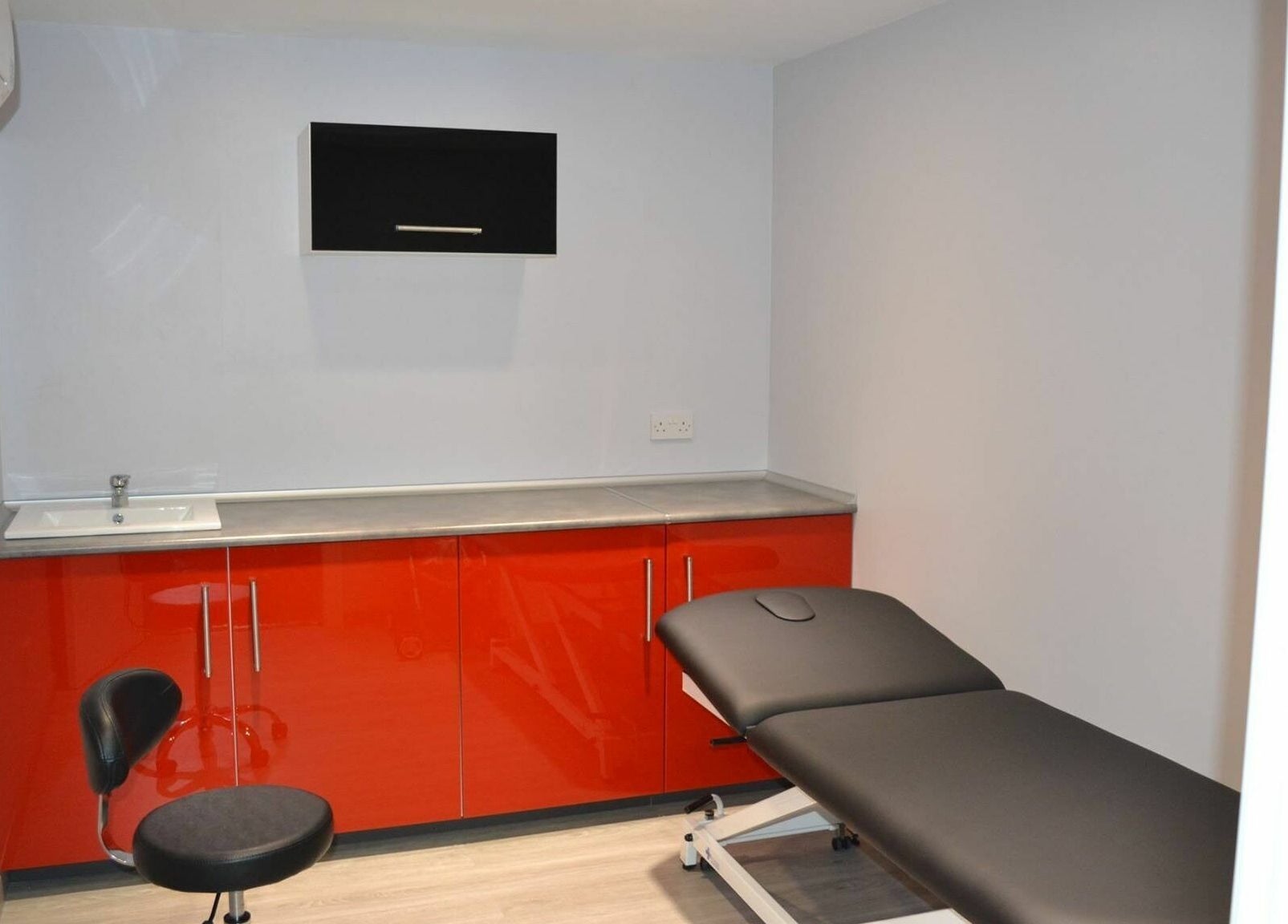 Sleek exam room at Activ Sports Medicine and Performance Clinic, Gibraltar, GI with red cabinetry and treatment bed.