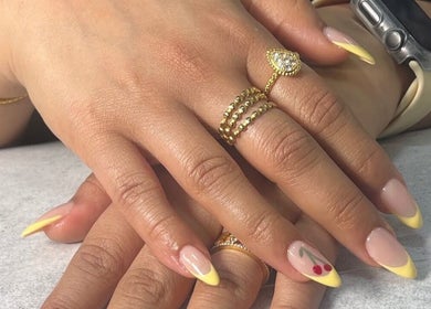 Elegant yellow-tipped nails with cherry design at Naya Saloon, Sanabis, Muḥāfaẓat Al-ʿāṣimah, BH.