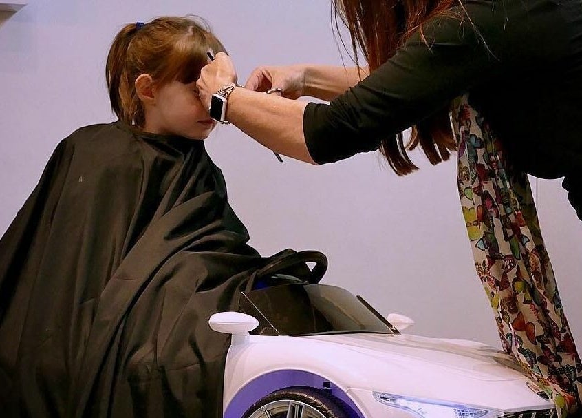 Hairdresser styling child's hair in car seat at The Salt Room, Sowerby Bridge, England, GB.