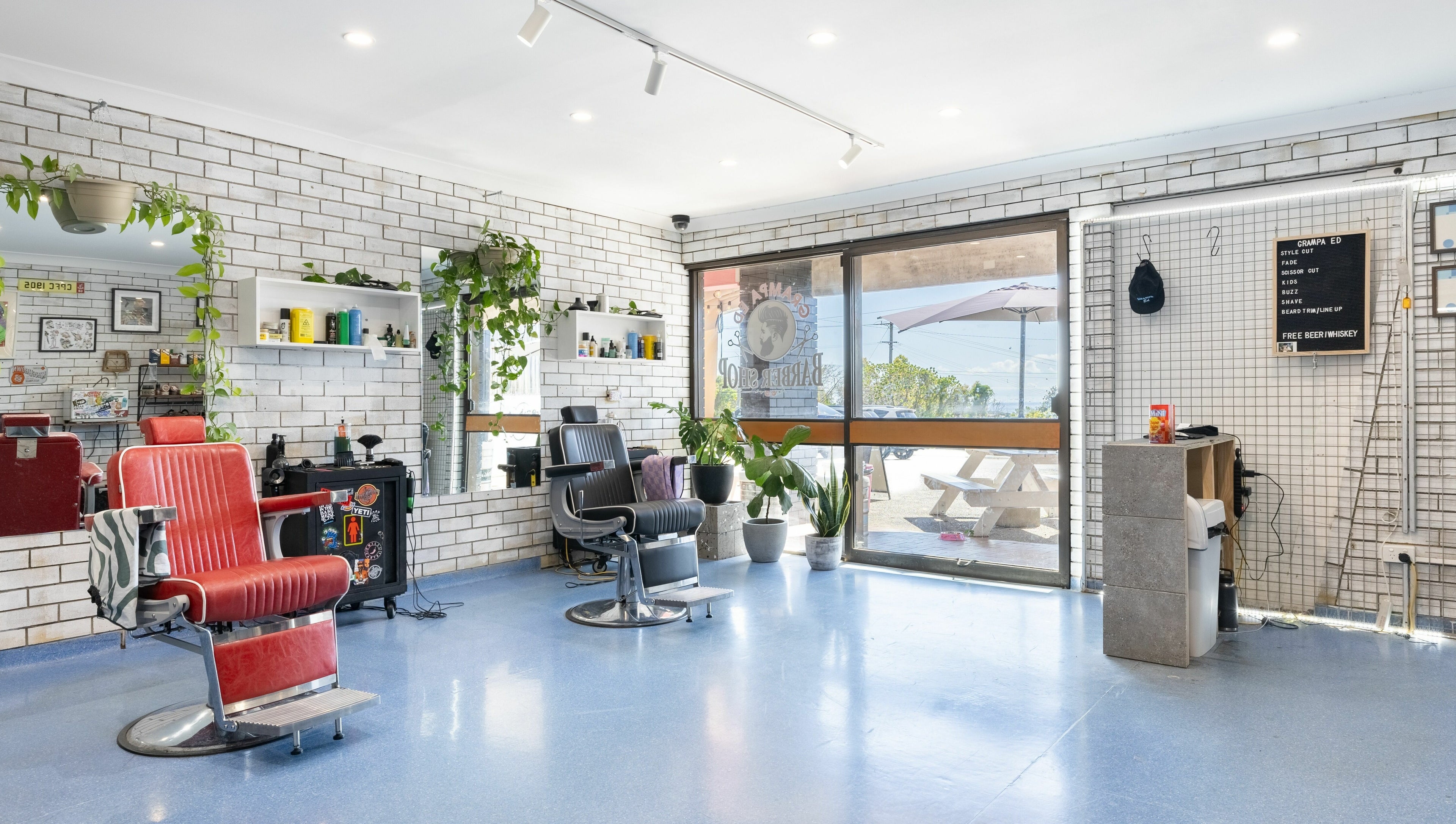 Modern barber shop interior at Grampa Ed, Banora Point, New South Wales, AU with red chairs and potted plants.
