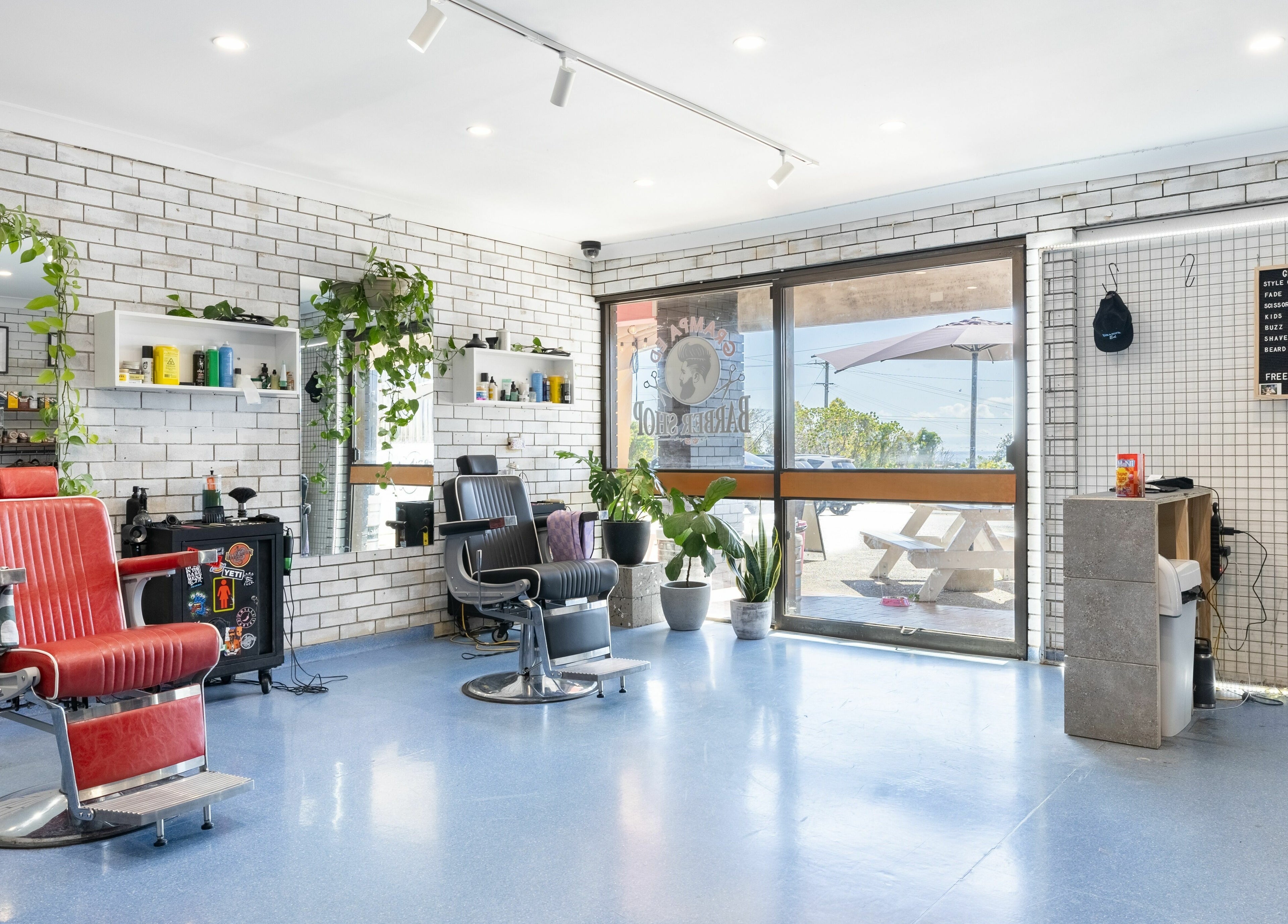 Modern barber shop interior at Grampa Ed, Banora Point, New South Wales, AU with red chairs and potted plants.