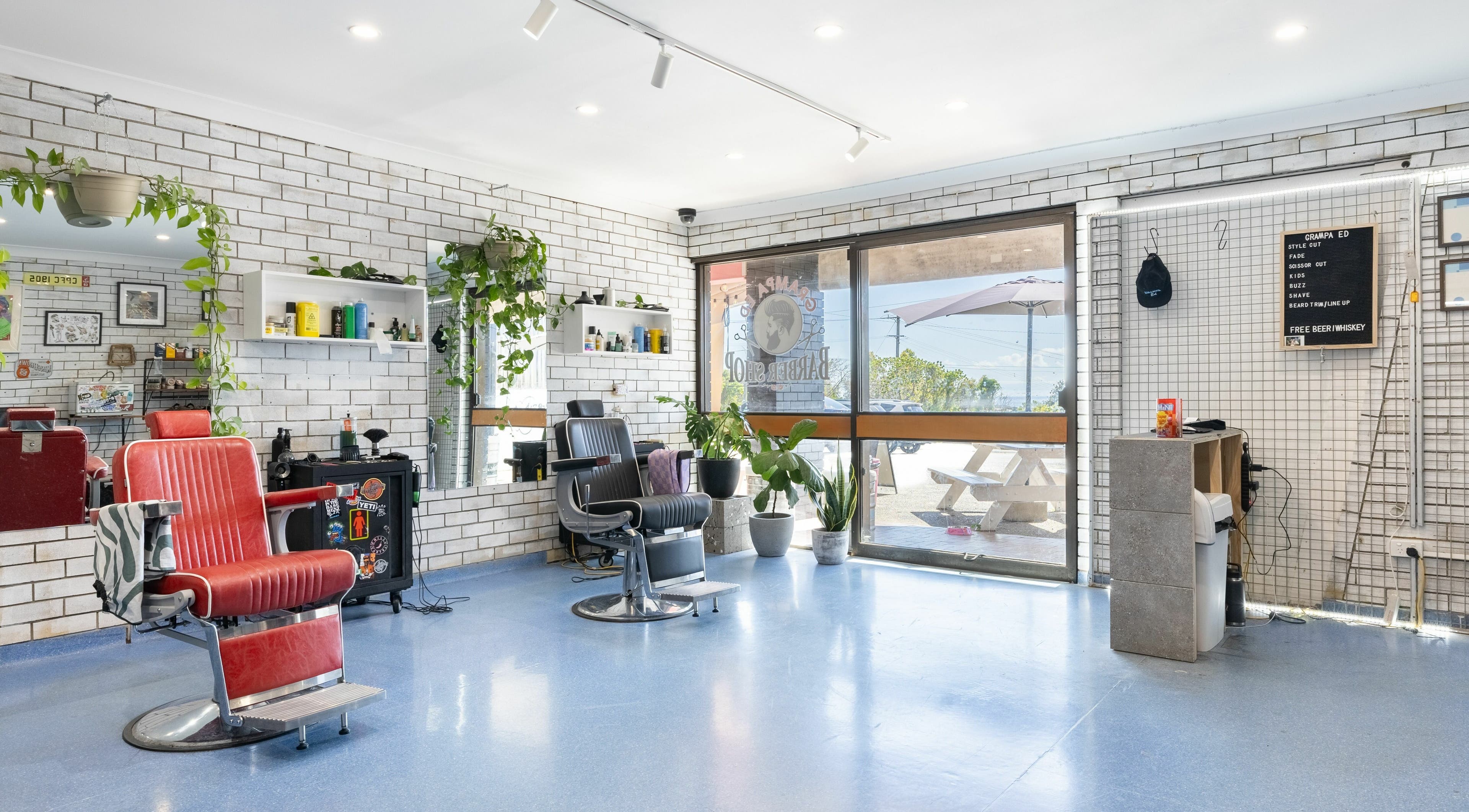 Modern barber shop interior at Grampa Ed, Banora Point, New South Wales, AU with red chairs and potted plants.