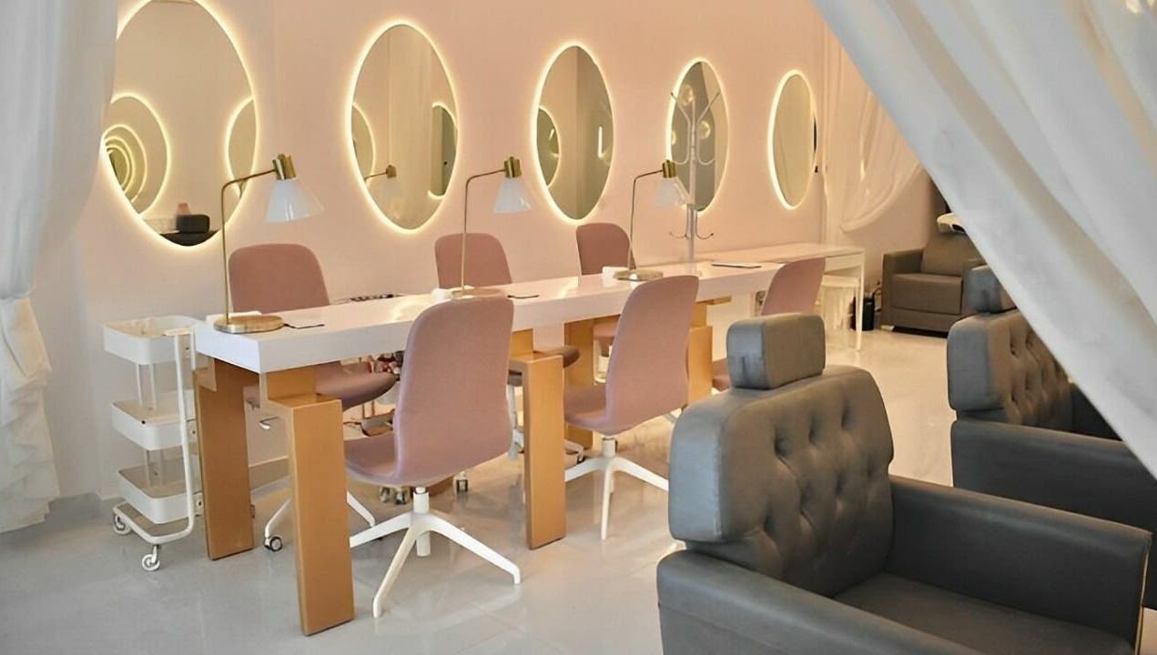 Chic nail salon interior at Antheia Enhance, Dehradun, Uttarakhand, IN with pink chairs and illuminated mirrors.