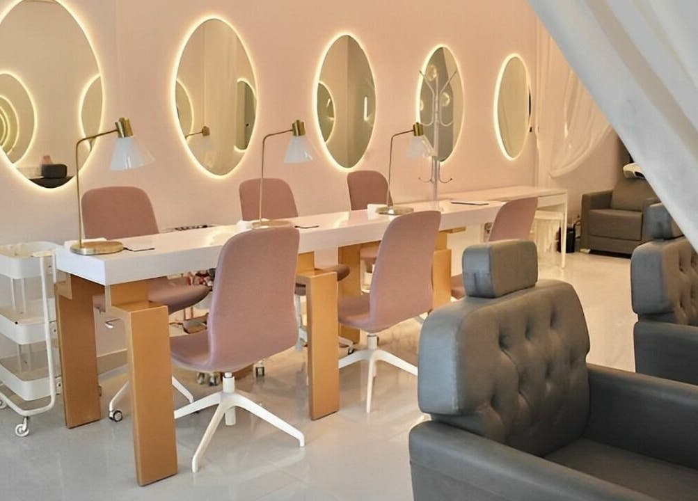 Chic nail salon interior at Antheia Enhance, Dehradun, Uttarakhand, IN with pink chairs and illuminated mirrors.