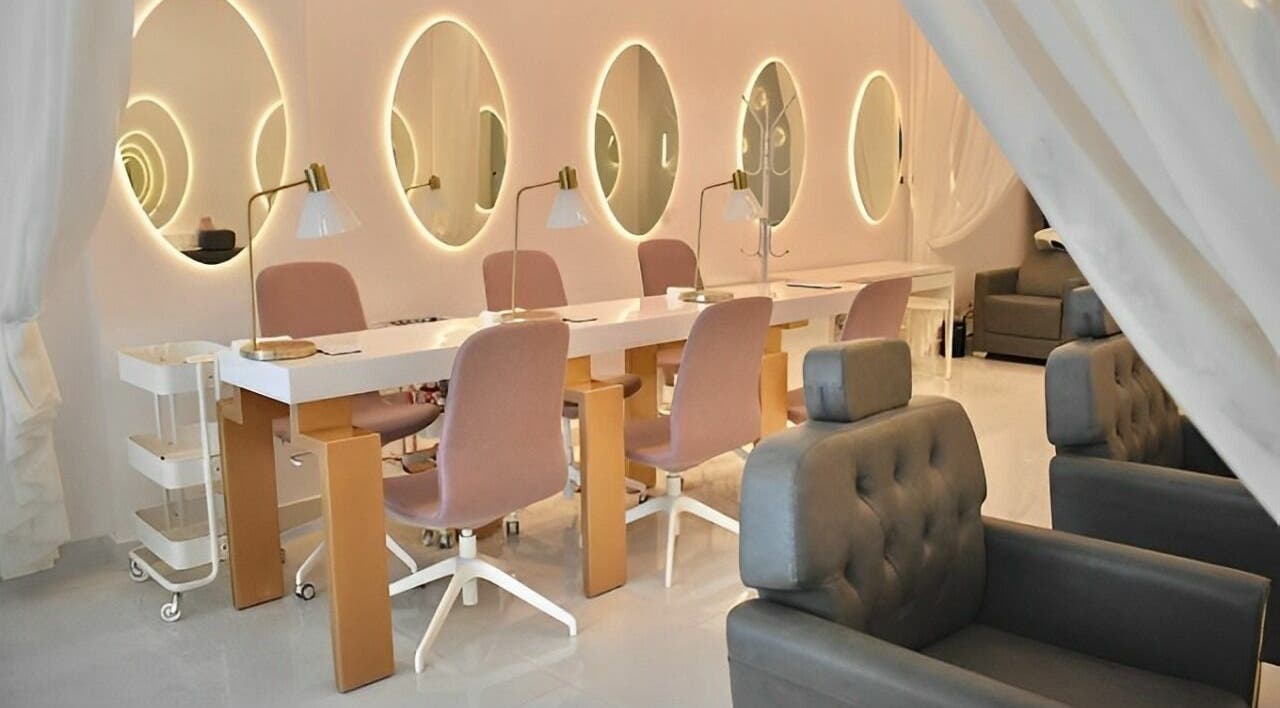 Chic nail salon interior at Antheia Enhance, Dehradun, Uttarakhand, IN with pink chairs and illuminated mirrors.