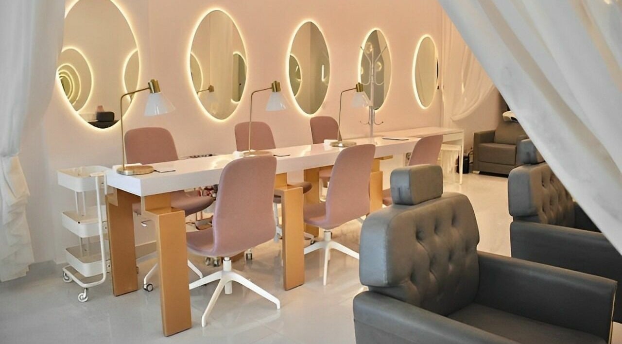 Chic nail salon interior at Antheia Enhance, Dehradun, Uttarakhand, IN with pink chairs and illuminated mirrors.