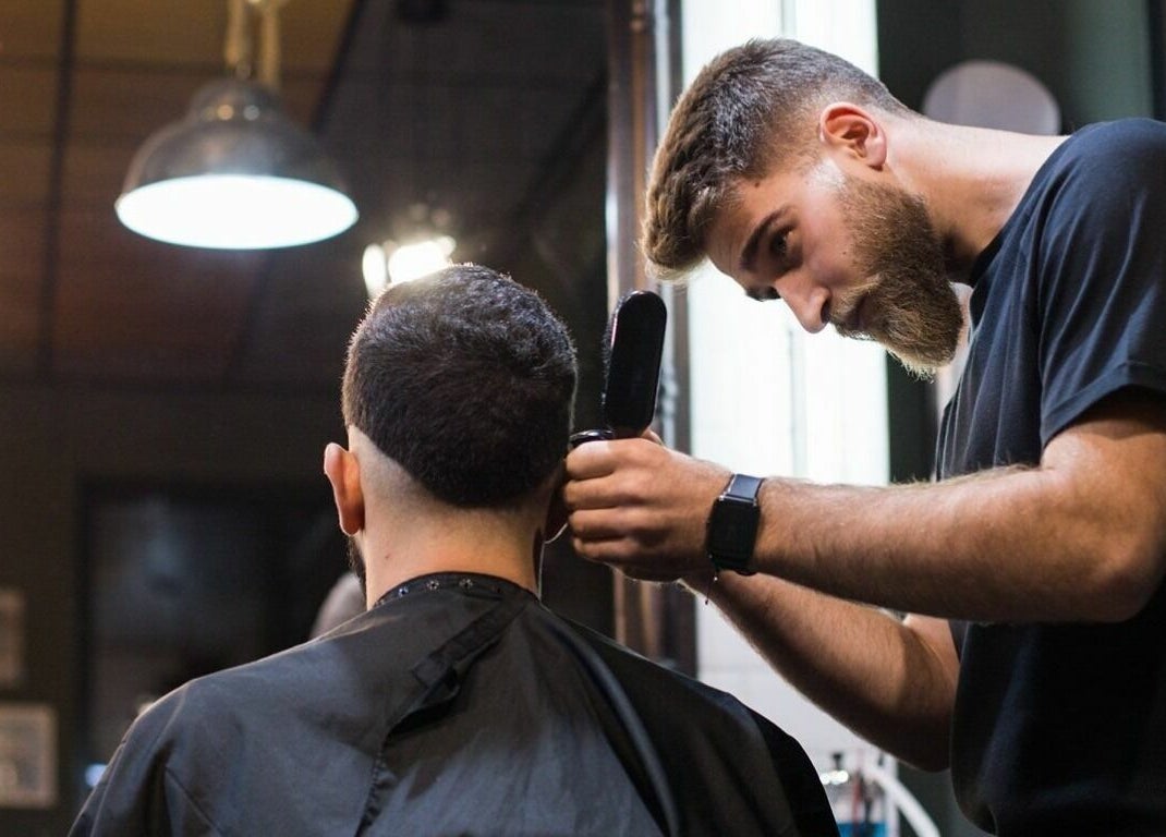 Frizer la Barber Society tunde un client în Cluj-Napoca, Județul Cluj, RO, sub o lumină elegantă.