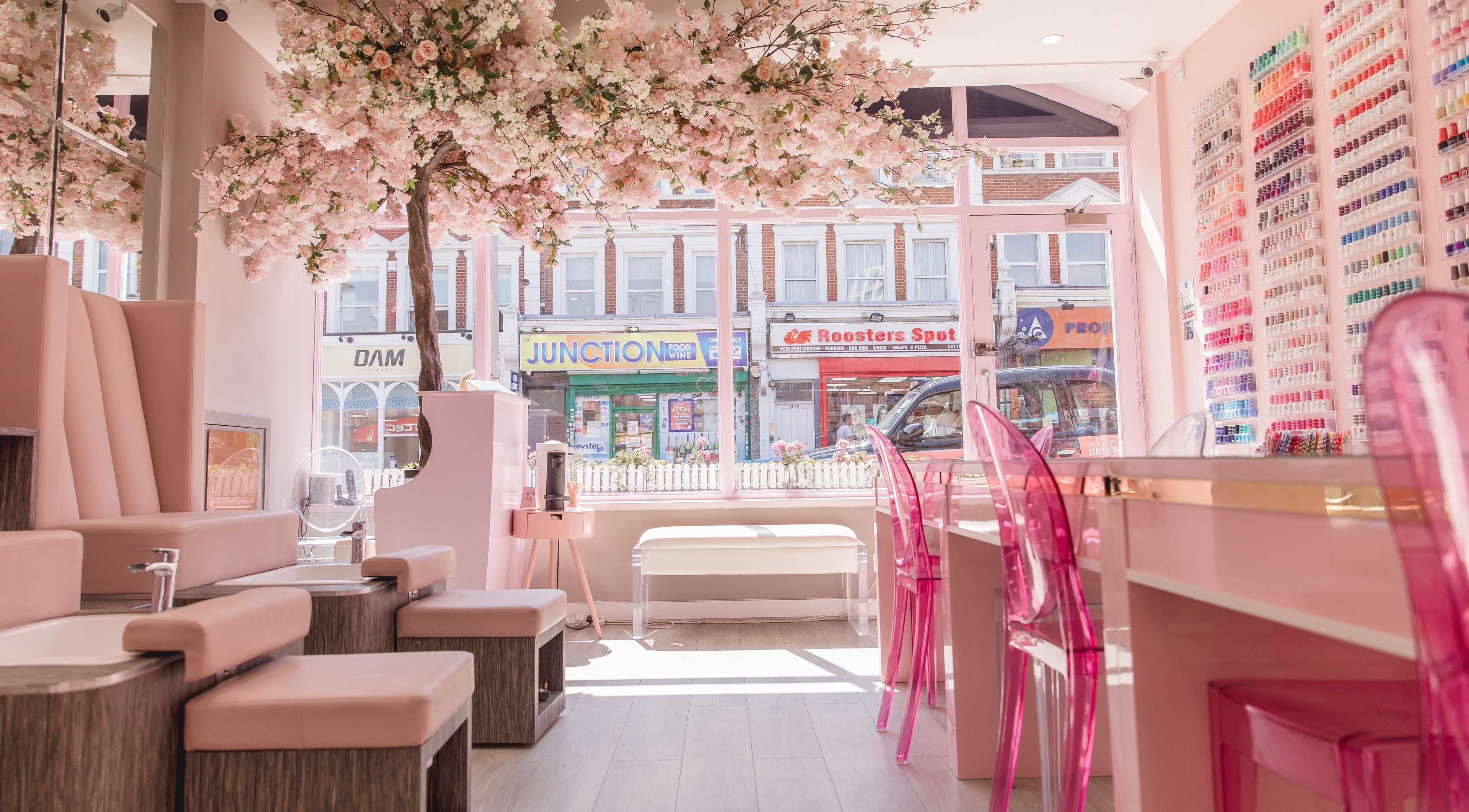 Elegant interior of Nail'd It Clapham salon in London, England, GB, featuring chic pink decor and nail polish display.