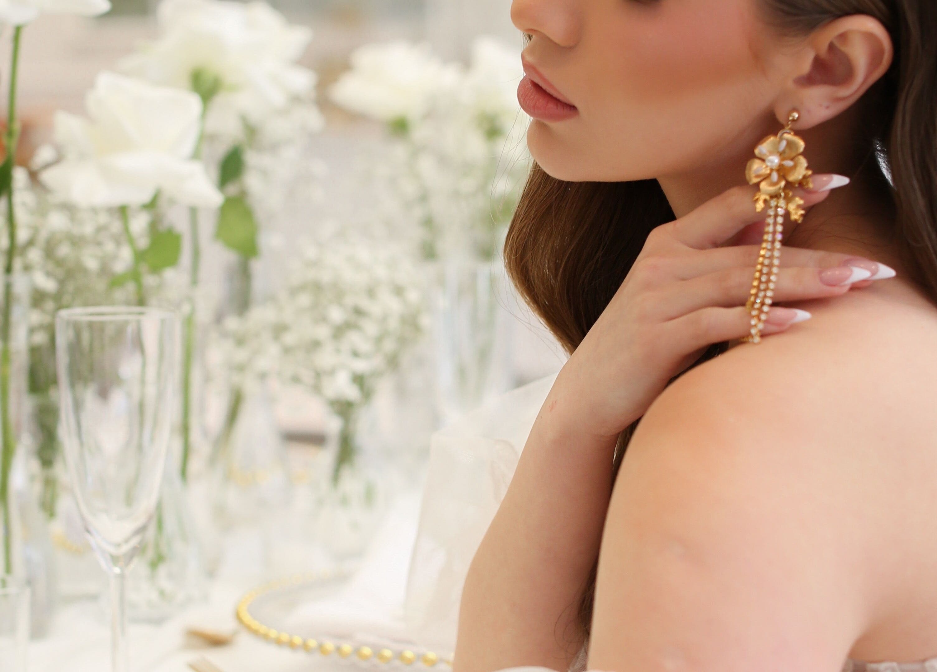 Woman with gold floral earrings at Glam me up Toronto, Vaughan, Ontario, CA. Surrounded by delicate white roses.
