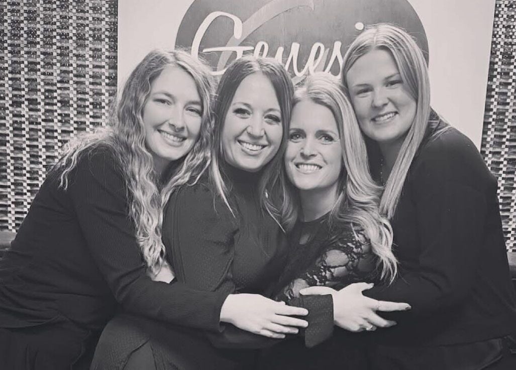 Happy team at Genesis Salon and Spa in Boscobel, Wisconsin, US, embracing in front of logo.