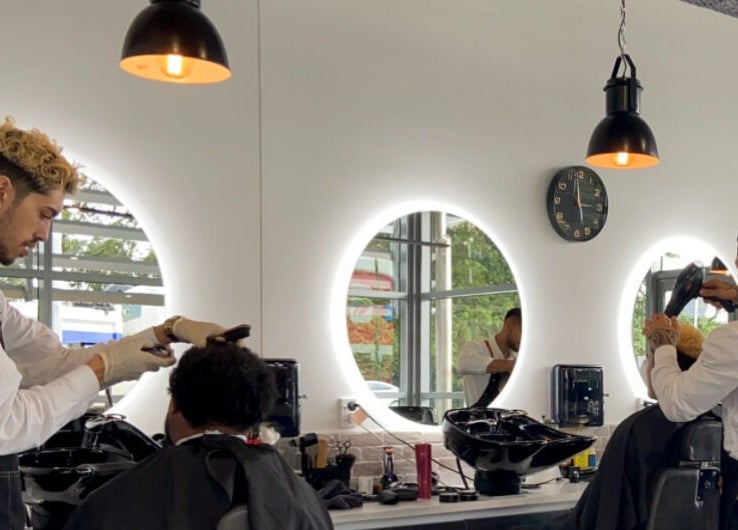 Barbers giving haircuts at Kirkwoods Barbers Stoneridge in Auckland, Auckland, NZ. Modern, well-lit salon.