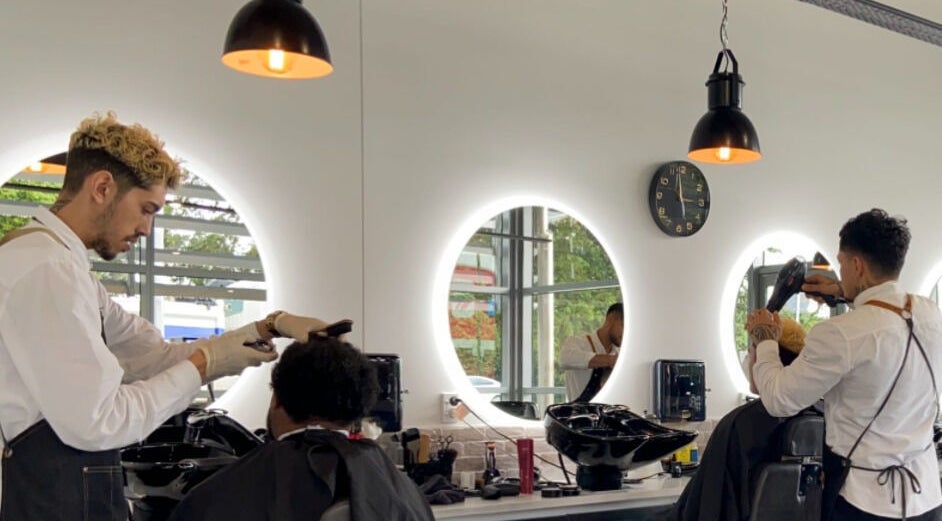 Barbers giving haircuts at Kirkwoods Barbers Stoneridge in Auckland, Auckland, NZ. Modern, well-lit salon.