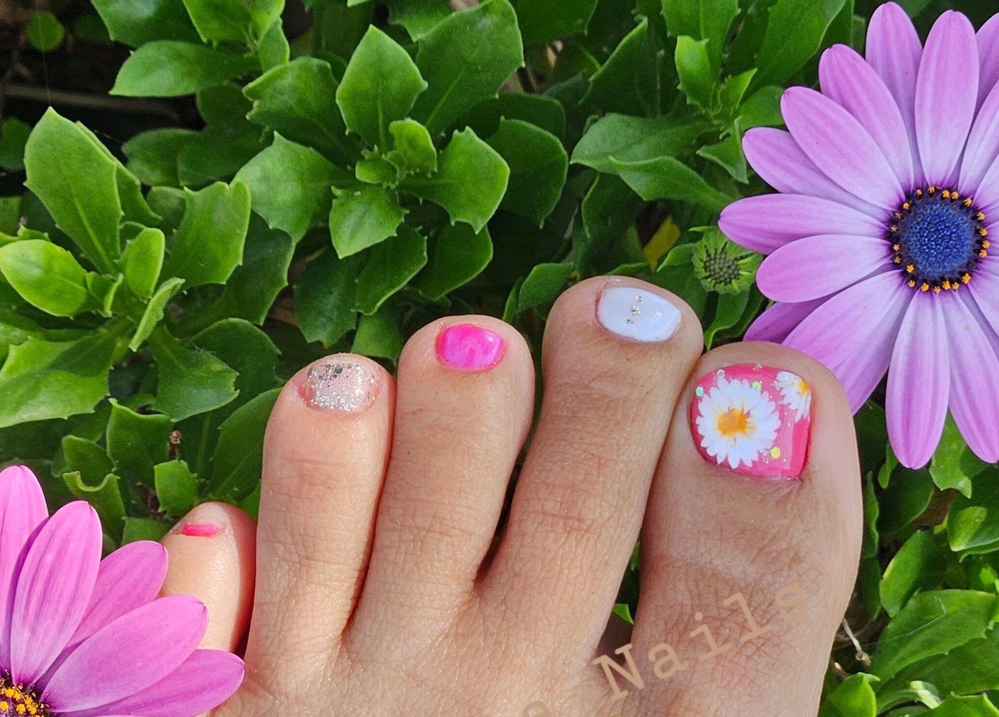 Vibrant floral pedicure design at Fortuna Nails, Worthing, England, GB, surrounded by purple flowers.