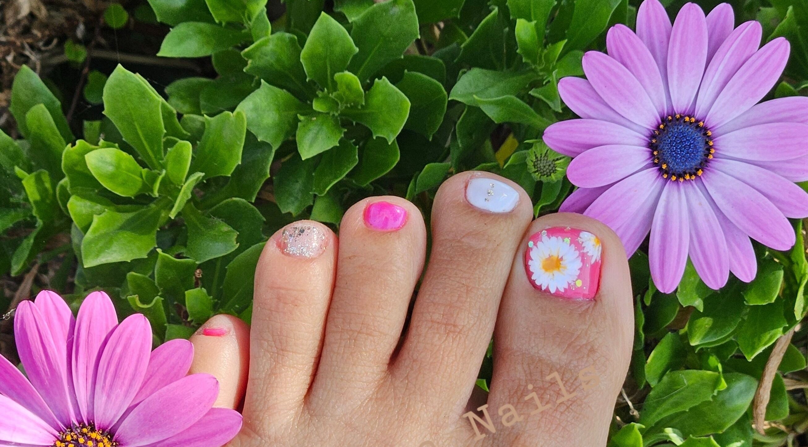 Vibrant floral pedicure design at Fortuna Nails, Worthing, England, GB, surrounded by purple flowers.