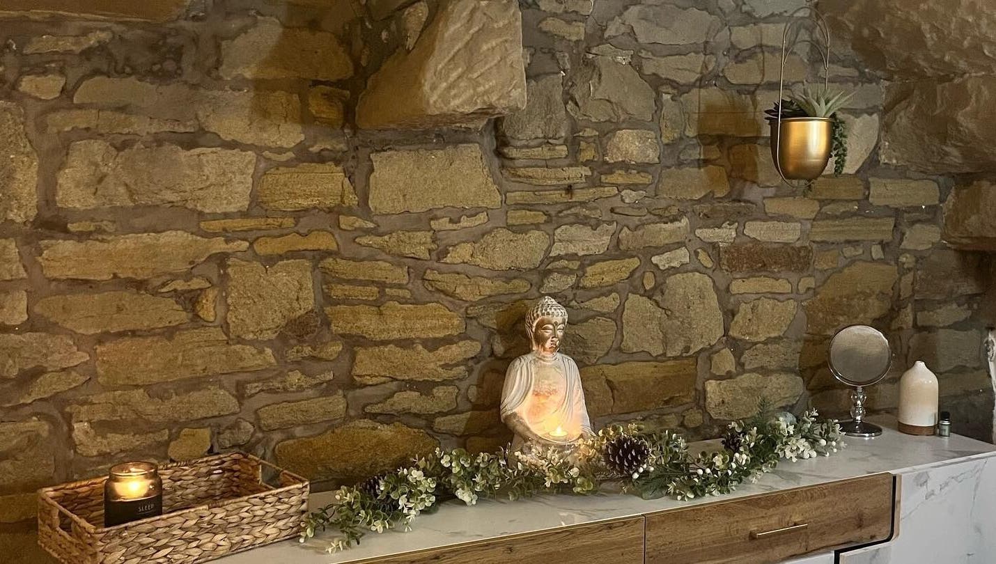 Serene stone wall with a Buddha statue at My Treat, Ramsbottom, England, GB. Candle-lit for calming ambiance.
