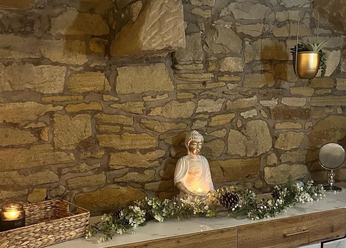 Serene stone wall with a Buddha statue at My Treat, Ramsbottom, England, GB. Candle-lit for calming ambiance.