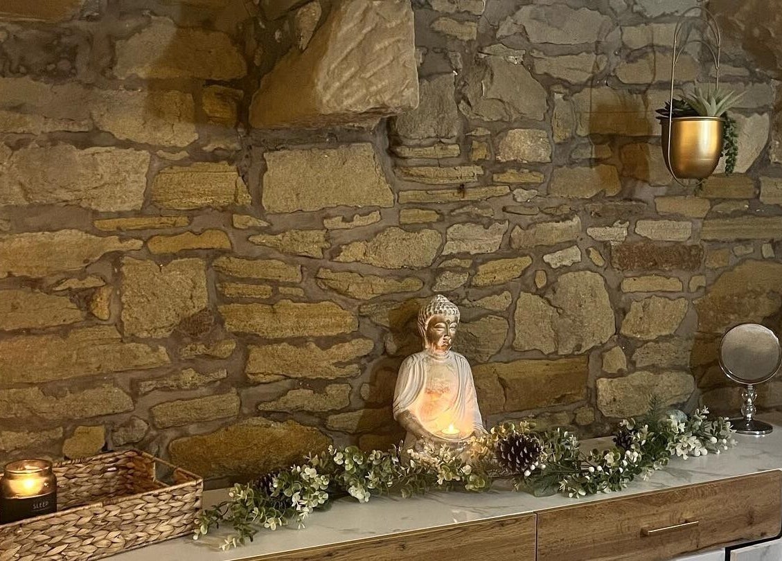 Serene stone wall with a Buddha statue at My Treat, Ramsbottom, England, GB. Candle-lit for calming ambiance.