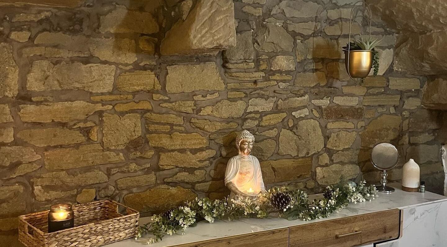 Serene stone wall with a Buddha statue at My Treat, Ramsbottom, England, GB. Candle-lit for calming ambiance.