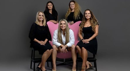 Team at Hayley Maree's Beauty Howick, Auckland, NZ. Five women pose on a pink chair, smiling.