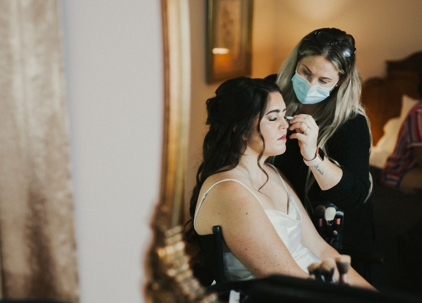 Makeup artist at Hill Hair and Makeup in Goderich, Ontario, CA enhances a client's beauty in a cozy setting.