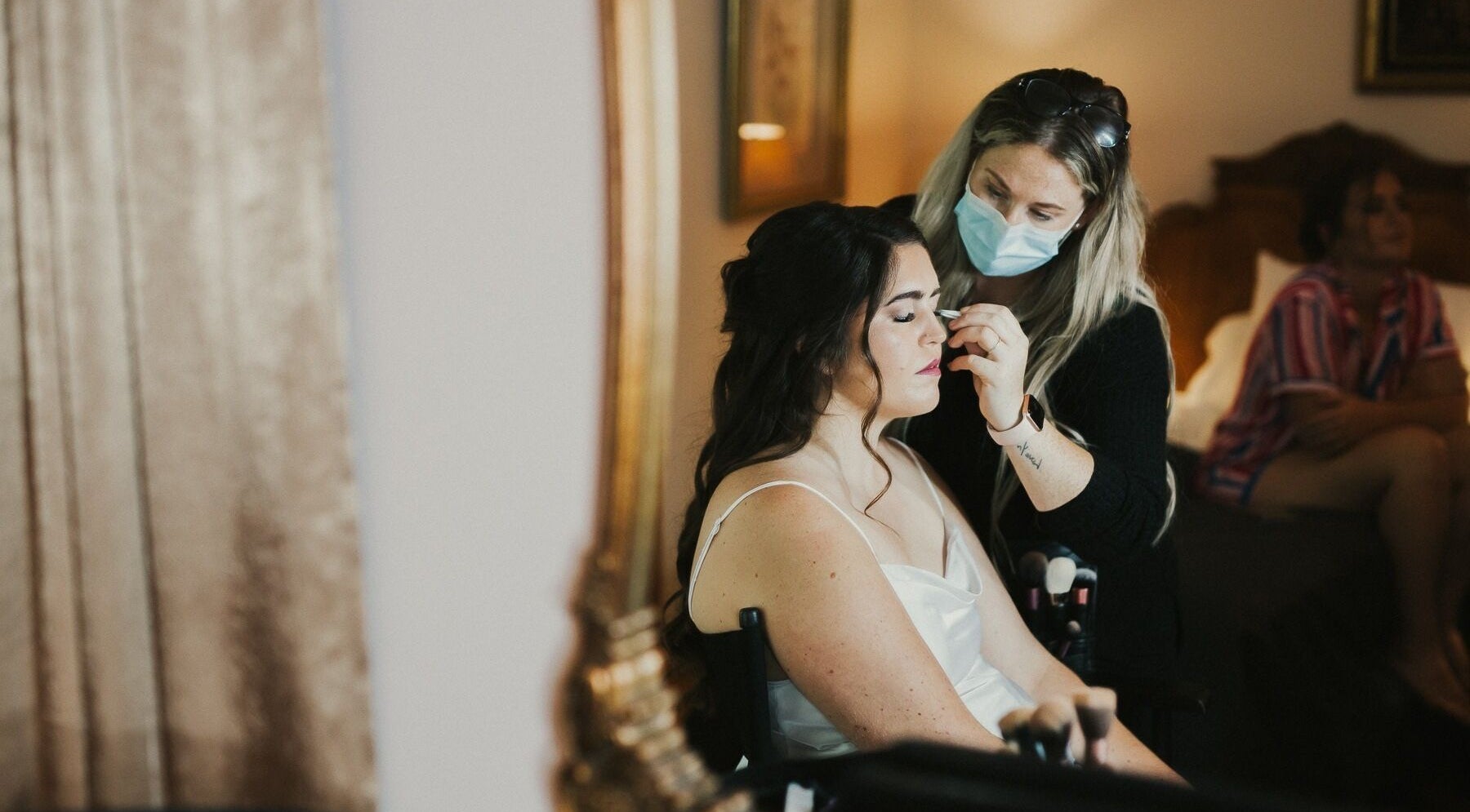 Makeup artist at Hill Hair and Makeup in Goderich, Ontario, CA enhances a client's beauty in a cozy setting.