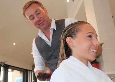 Stylist at Neil Curry Hairdressing Ltd, Cambridge, England, GB, attentively brushing a client's hair.