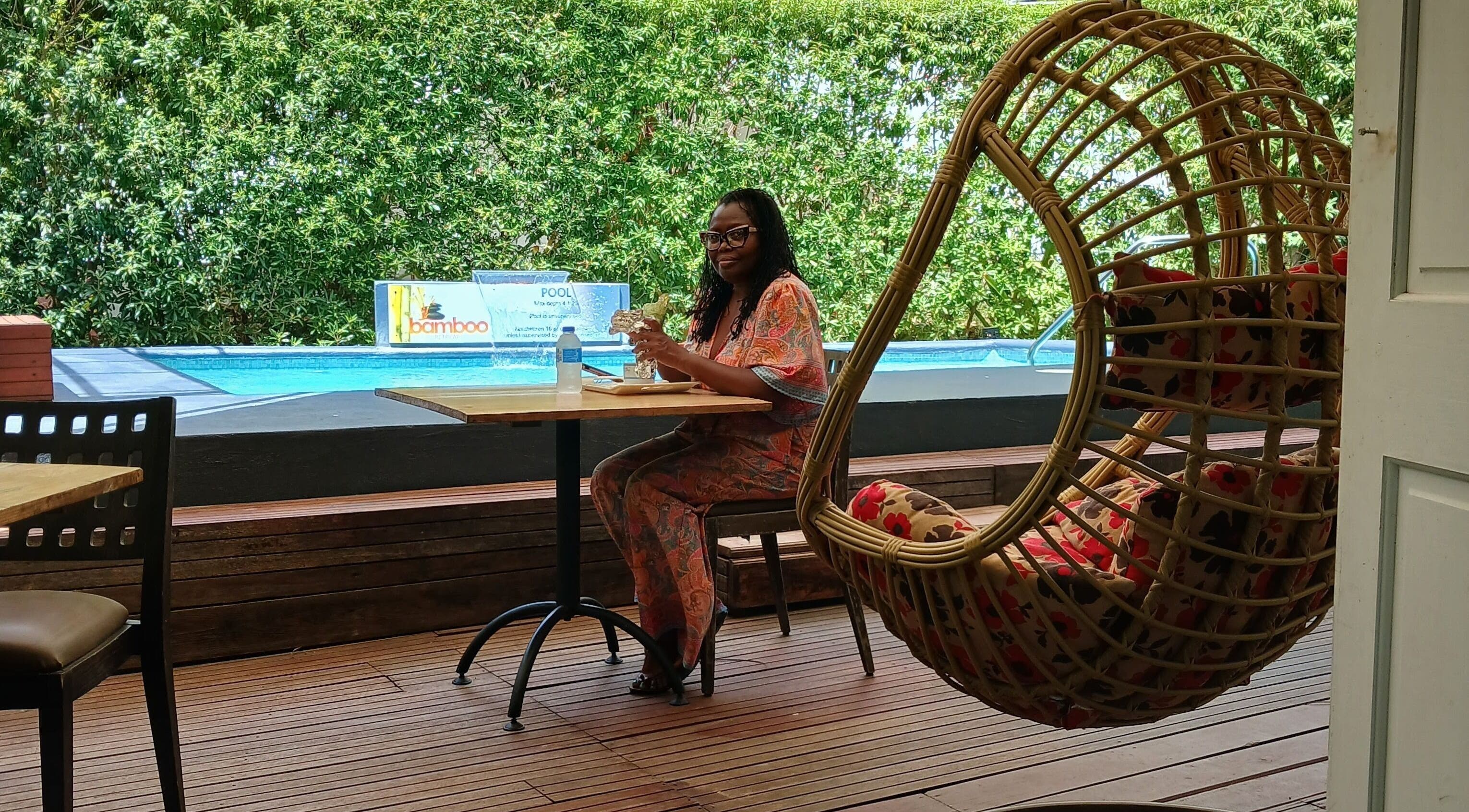 Woman relaxes at The Bamboo Retreat's patio in St. George, BB beside pool amid lush greenery.