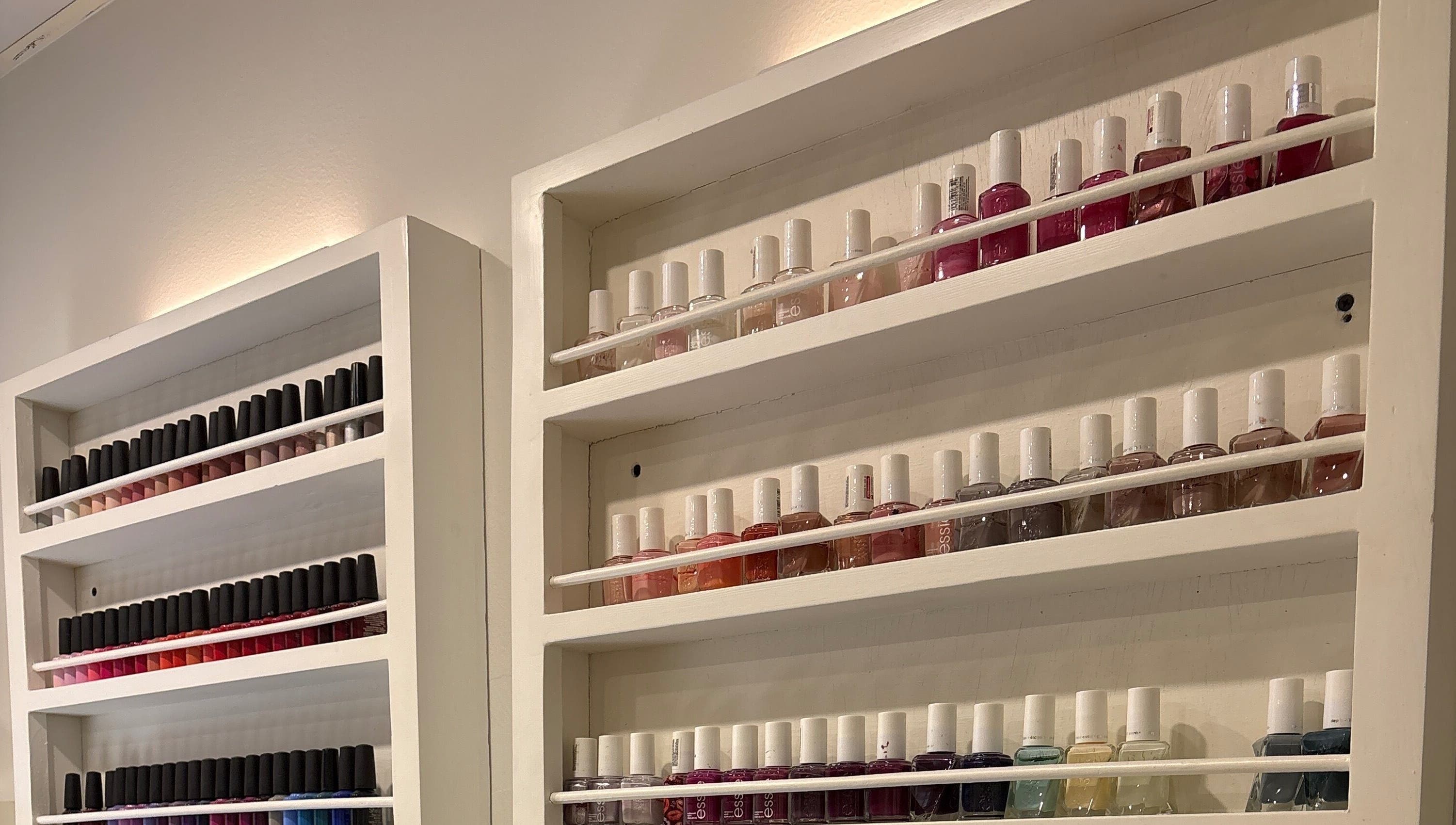 Nail polish display at The Little Spa, Westmoorings, TT. Vibrant colors arranged on white shelves.