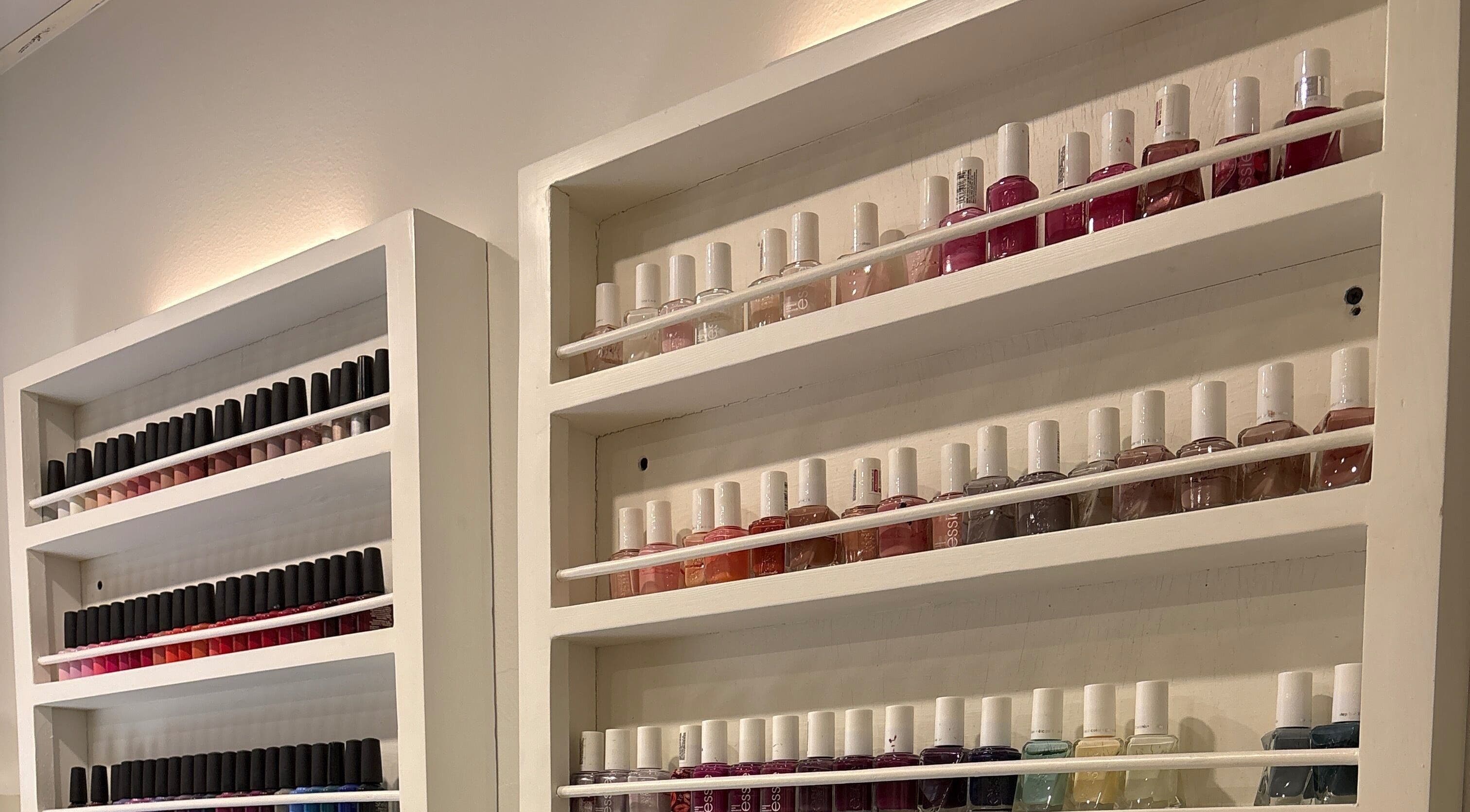 Nail polish display at The Little Spa, Westmoorings, TT. Vibrant colors arranged on white shelves.