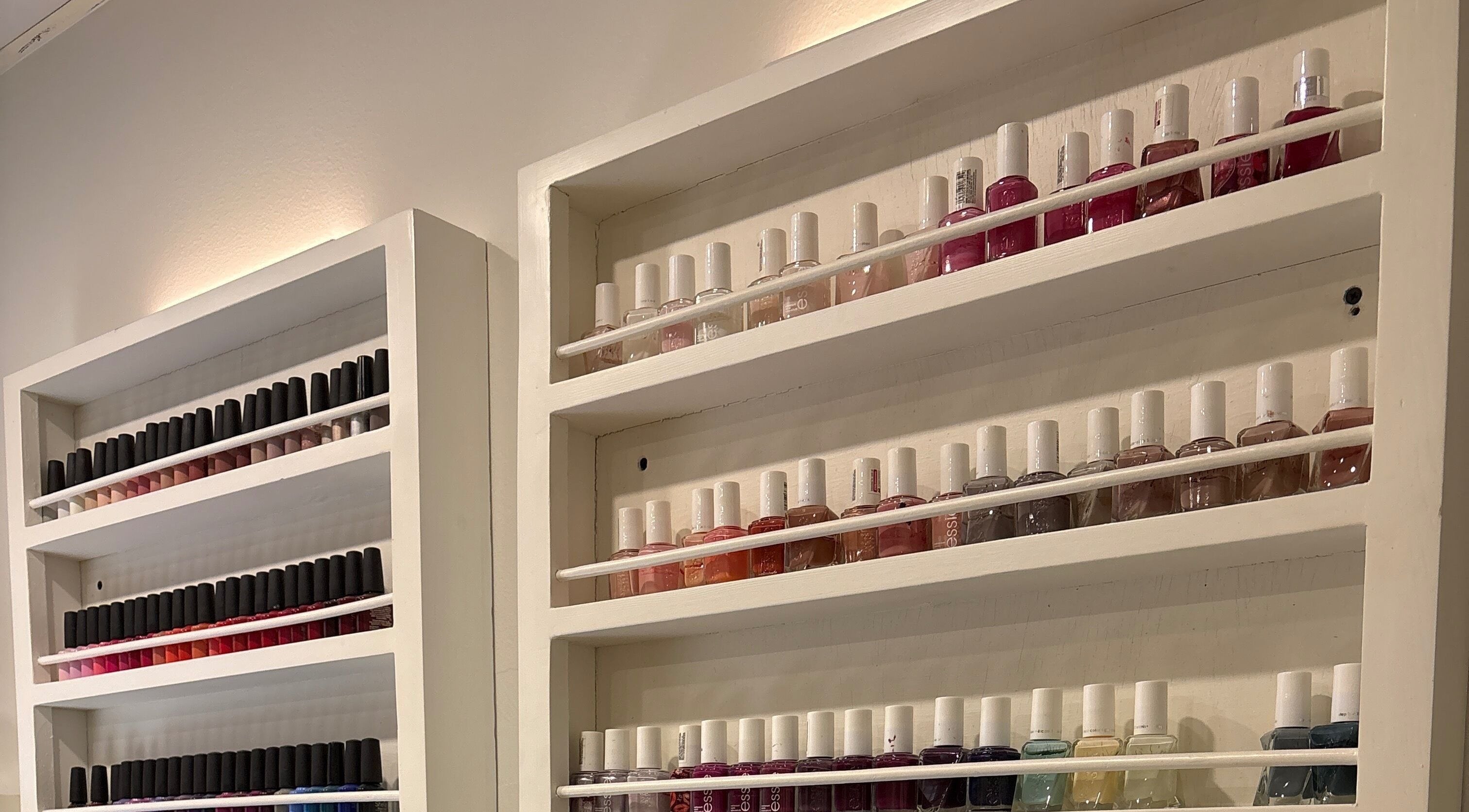 Nail polish display at The Little Spa, Westmoorings, TT. Vibrant colors arranged on white shelves.