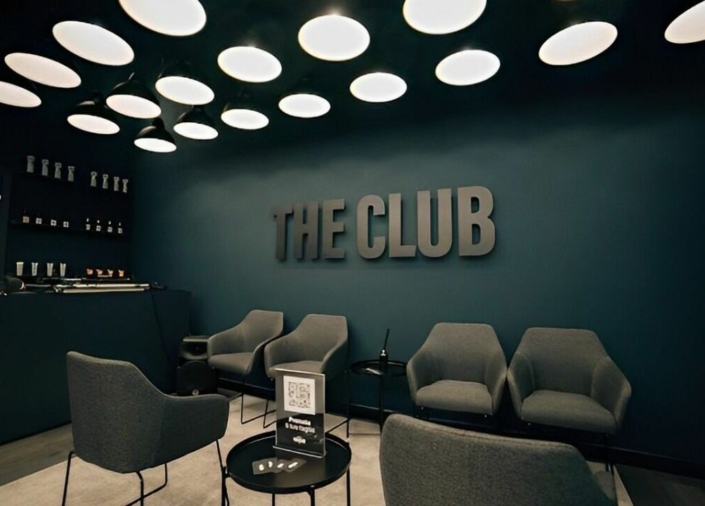Interno elegante di The Club Barbershop ad Adria, Veneto, IT con poltrone moderne e illuminazione soffusa.