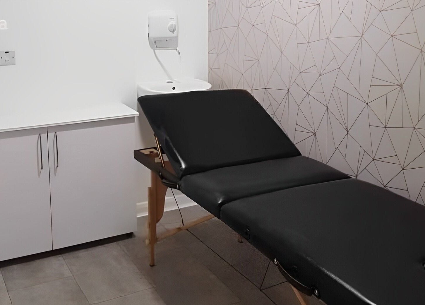 Treatment room at Roots, Windsor, England, GB featuring a sleek black massage table and geometric wallpaper.