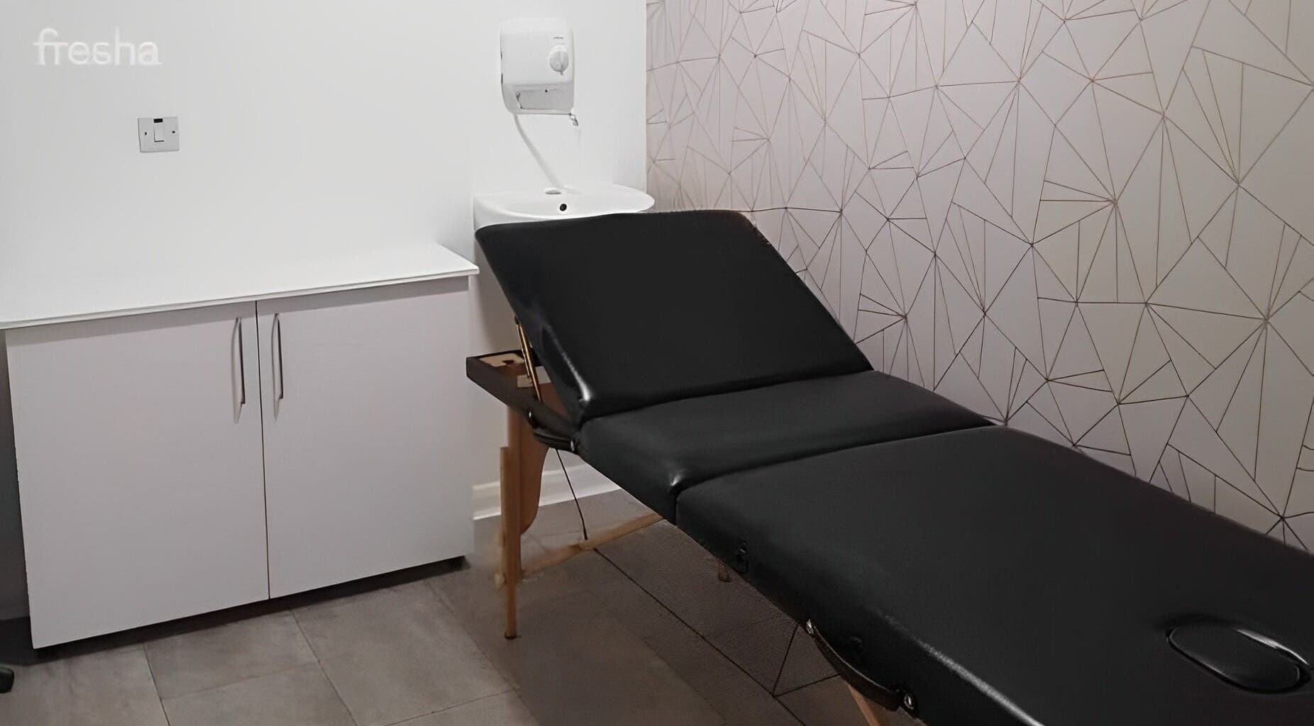Treatment room at Roots, Windsor, England, GB featuring a sleek black massage table and geometric wallpaper.