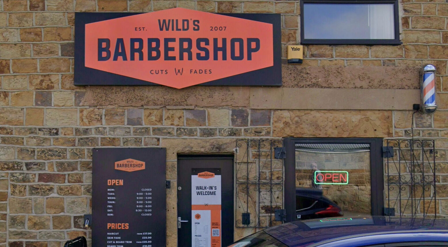 Front view of Wild's Barbershop in Sheffield, England, GB with its sign and open hours display.
