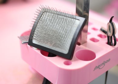 Pet grooming tools at Cuts For Pups, Melbourne, Victoria, AU. Includes a brush and scissors on a pink stand.