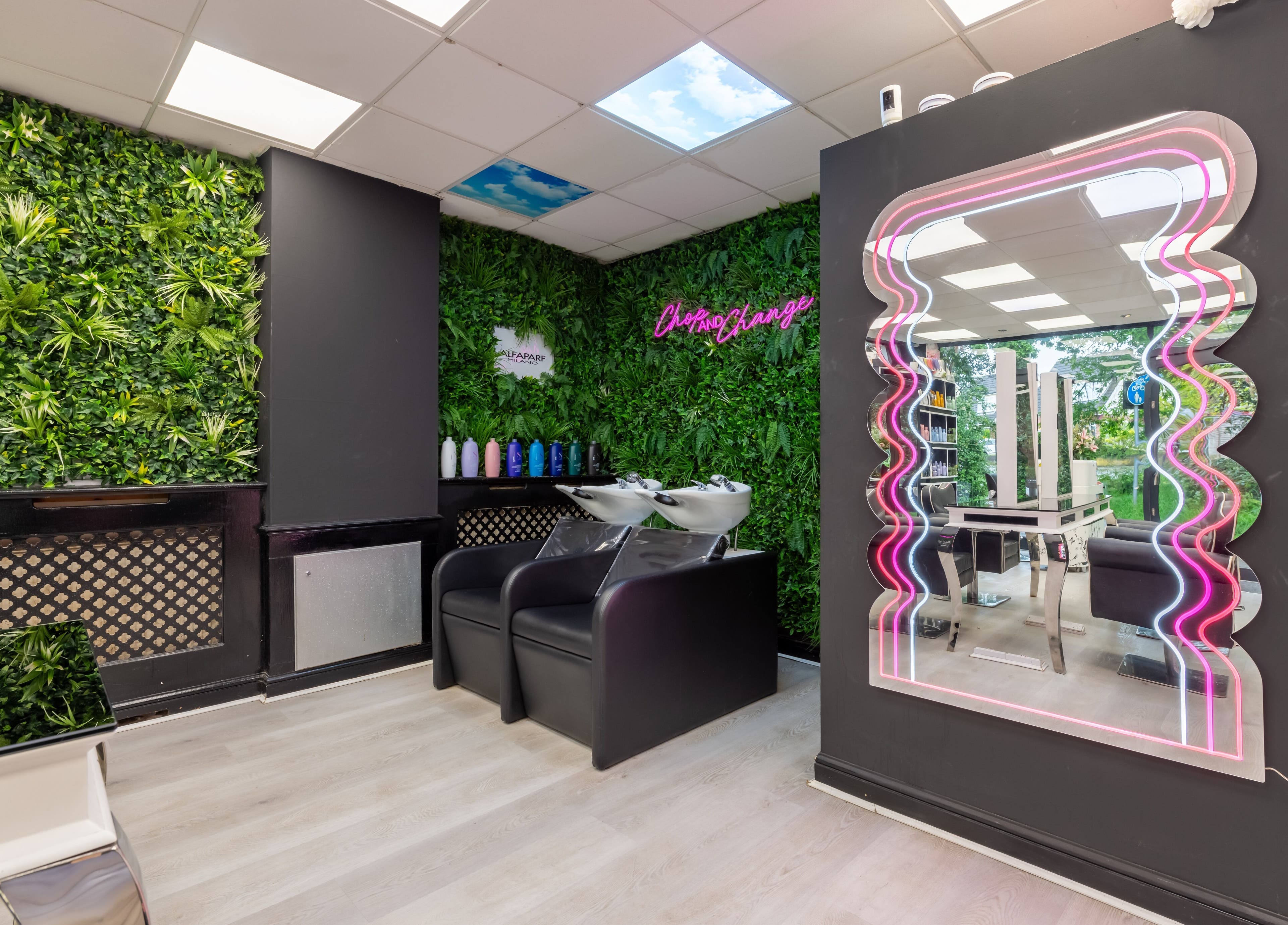 Chop and Change salon in Addlestone, England features vibrant greenery and a neon-framed mirror.