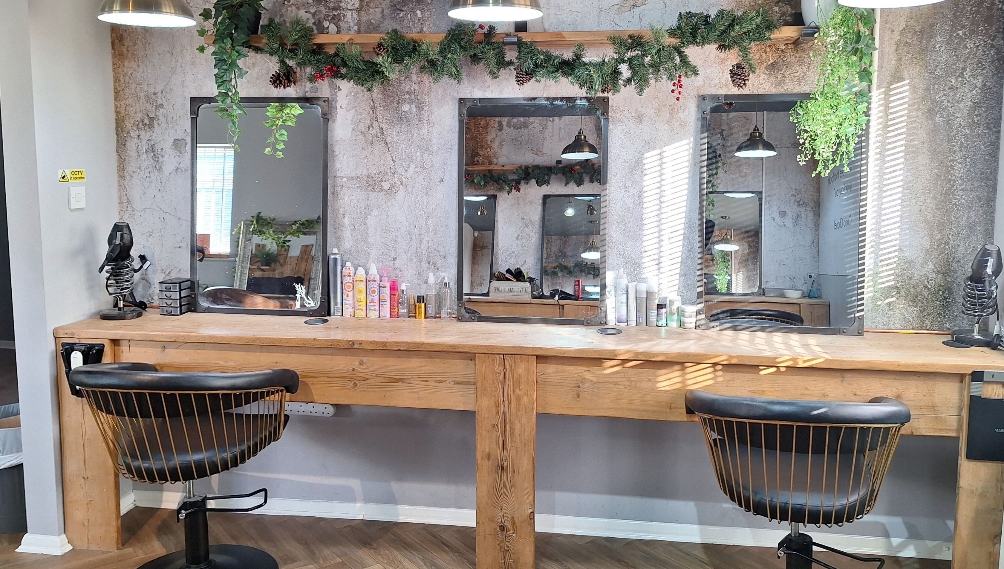 Rustic salon interior at CHEVEUX, Beighton, England, GB with wooden styling stations and decorative greenery.