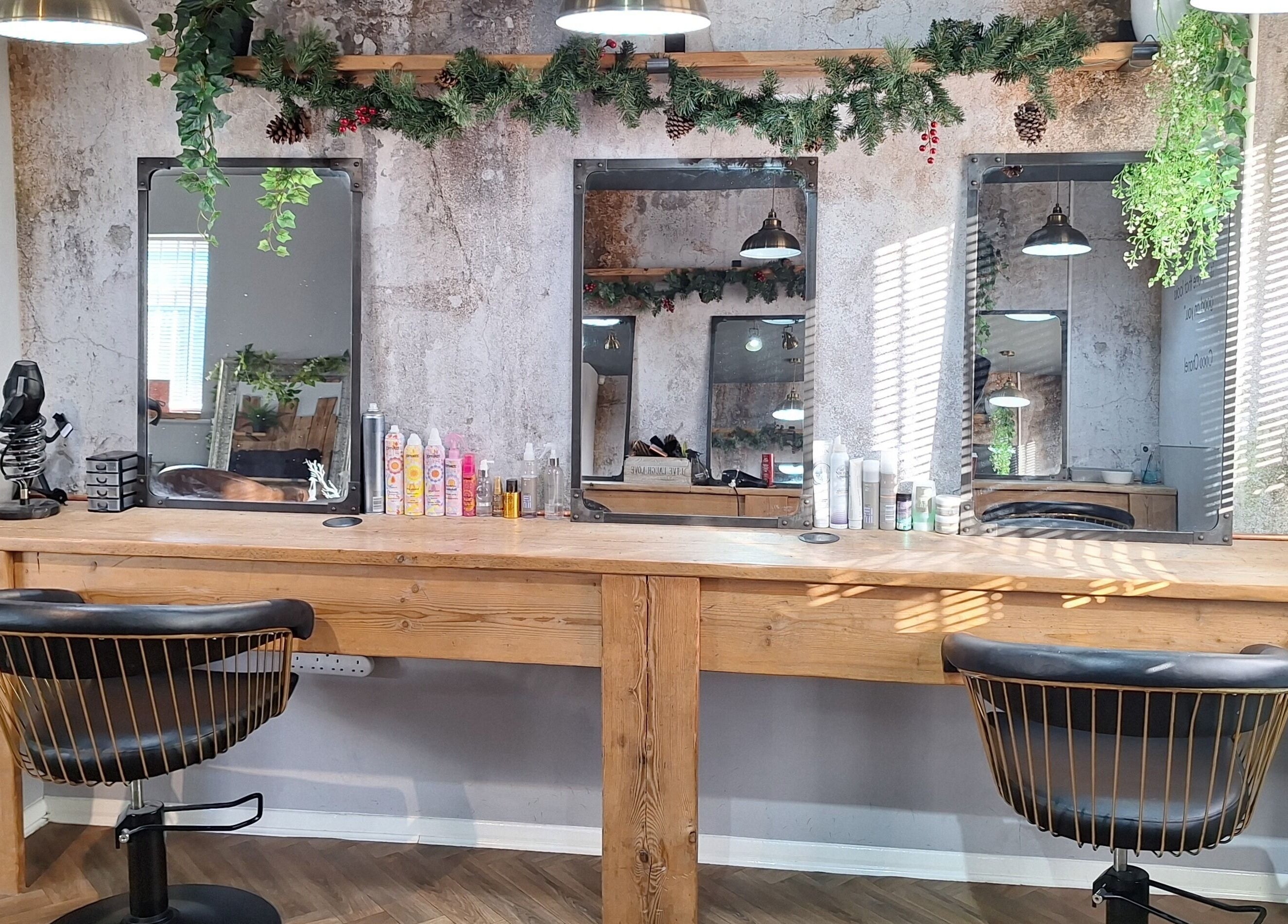 Rustic salon interior at CHEVEUX, Beighton, England, GB with wooden styling stations and decorative greenery.