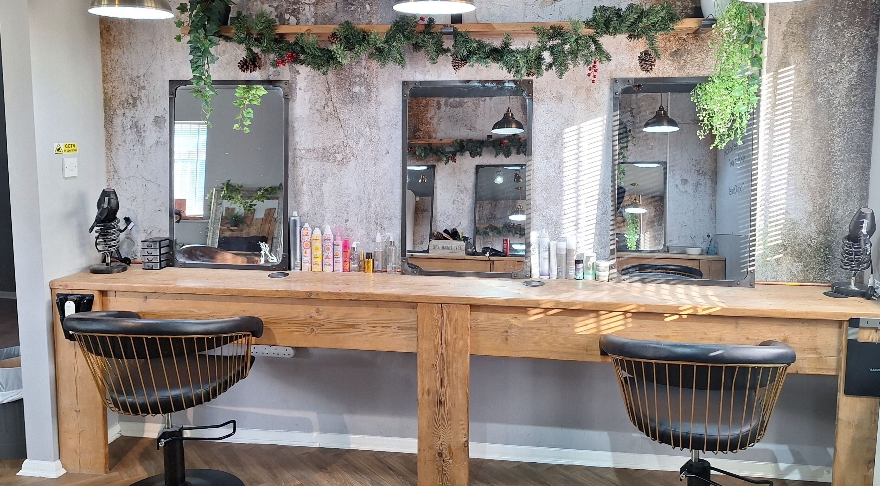 Rustic salon interior at CHEVEUX, Beighton, England, GB with wooden styling stations and decorative greenery.