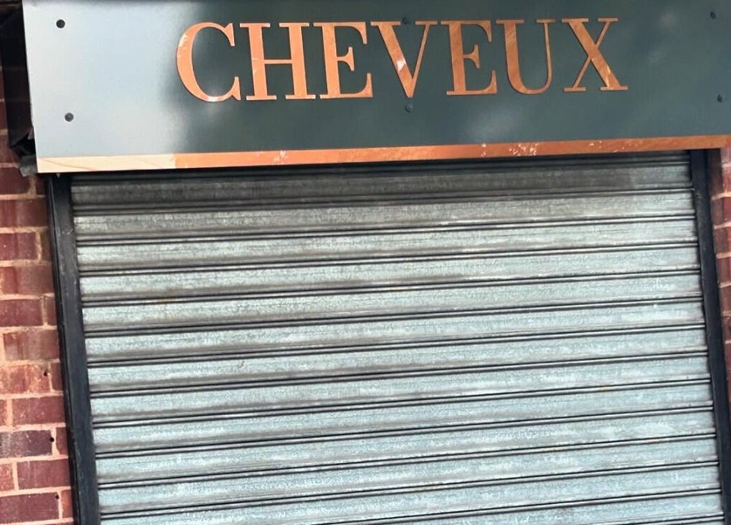 Front view of CHEVEUX salon entrance, Beighton, England, GB, featuring a sleek sign above a closed shutter.