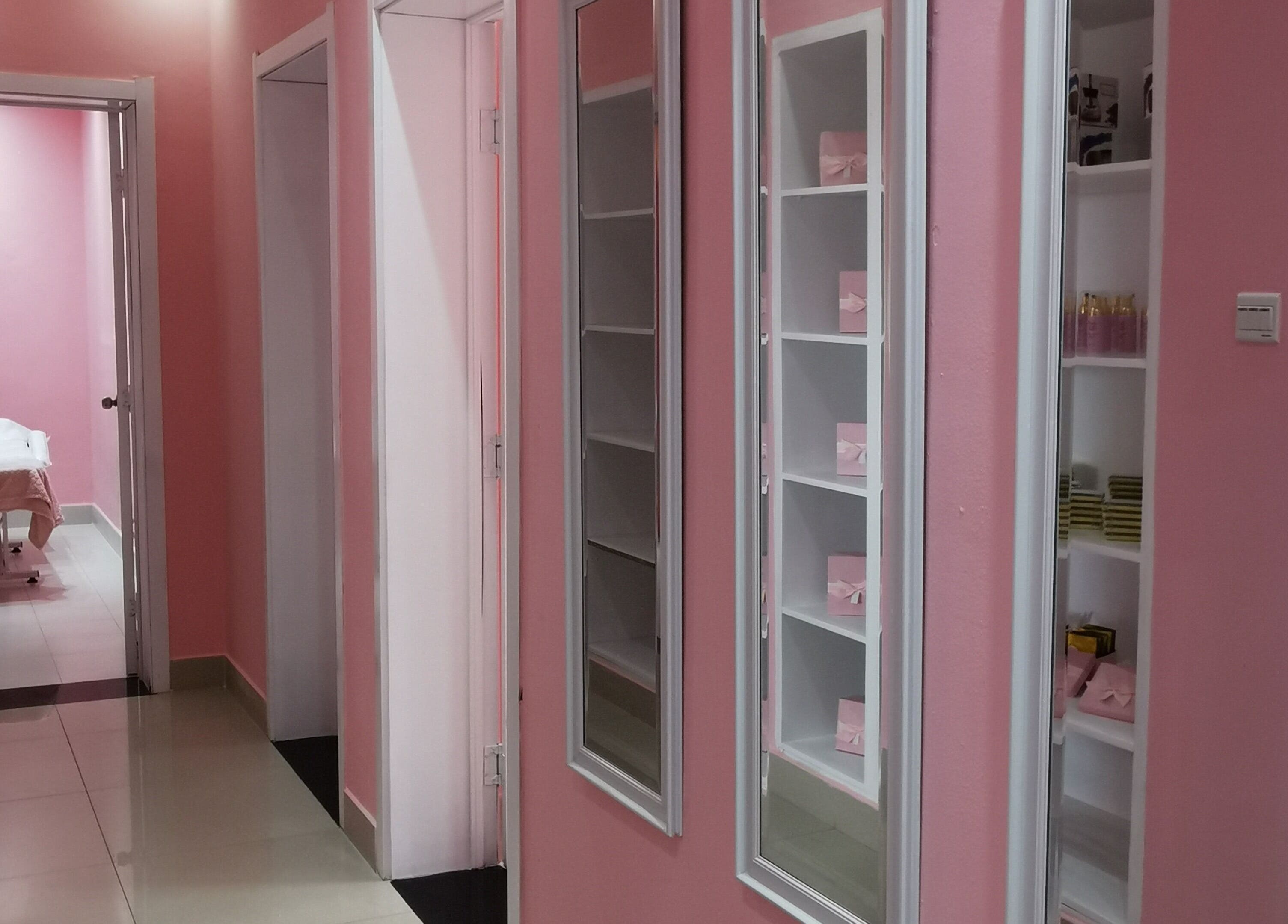 Corredor rosa de beleza no Rostos, Luanda, Luanda, AO com prateleiras e sala de tratamento ao fundo.