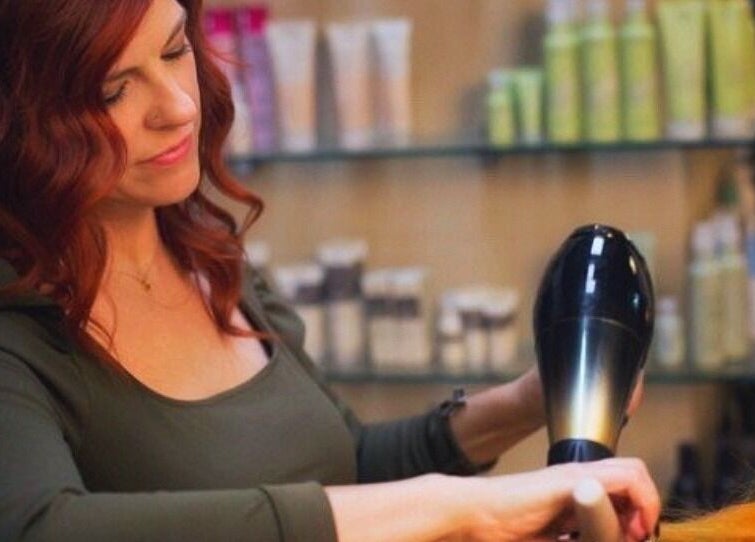 Stylist at Glendale Arts+Salon in Chicago, Illinois, US, expertly blow-drying vibrant red hair.