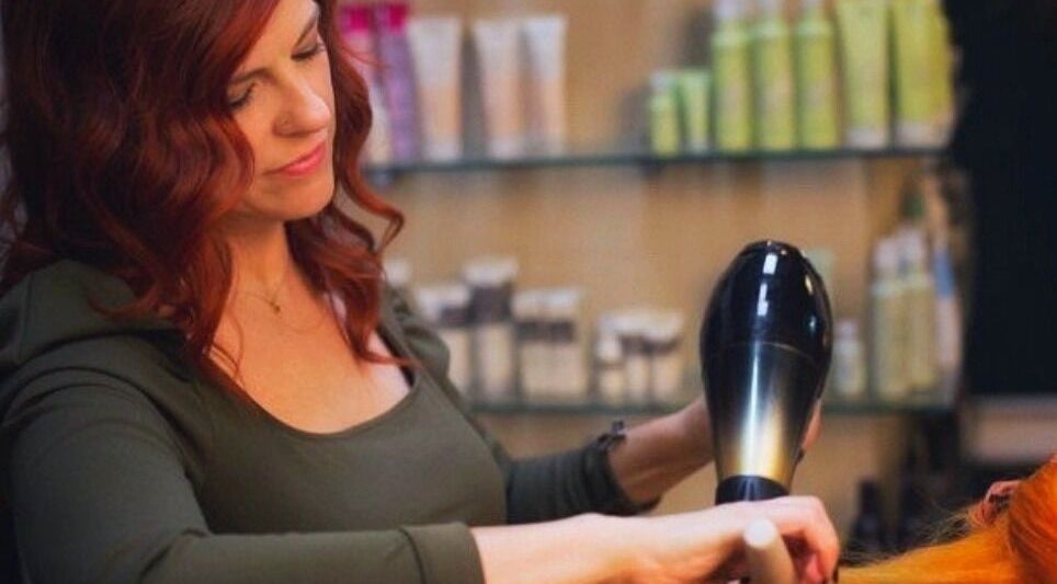 Stylist at Glendale Arts+Salon in Chicago, Illinois, US, expertly blow-drying vibrant red hair.