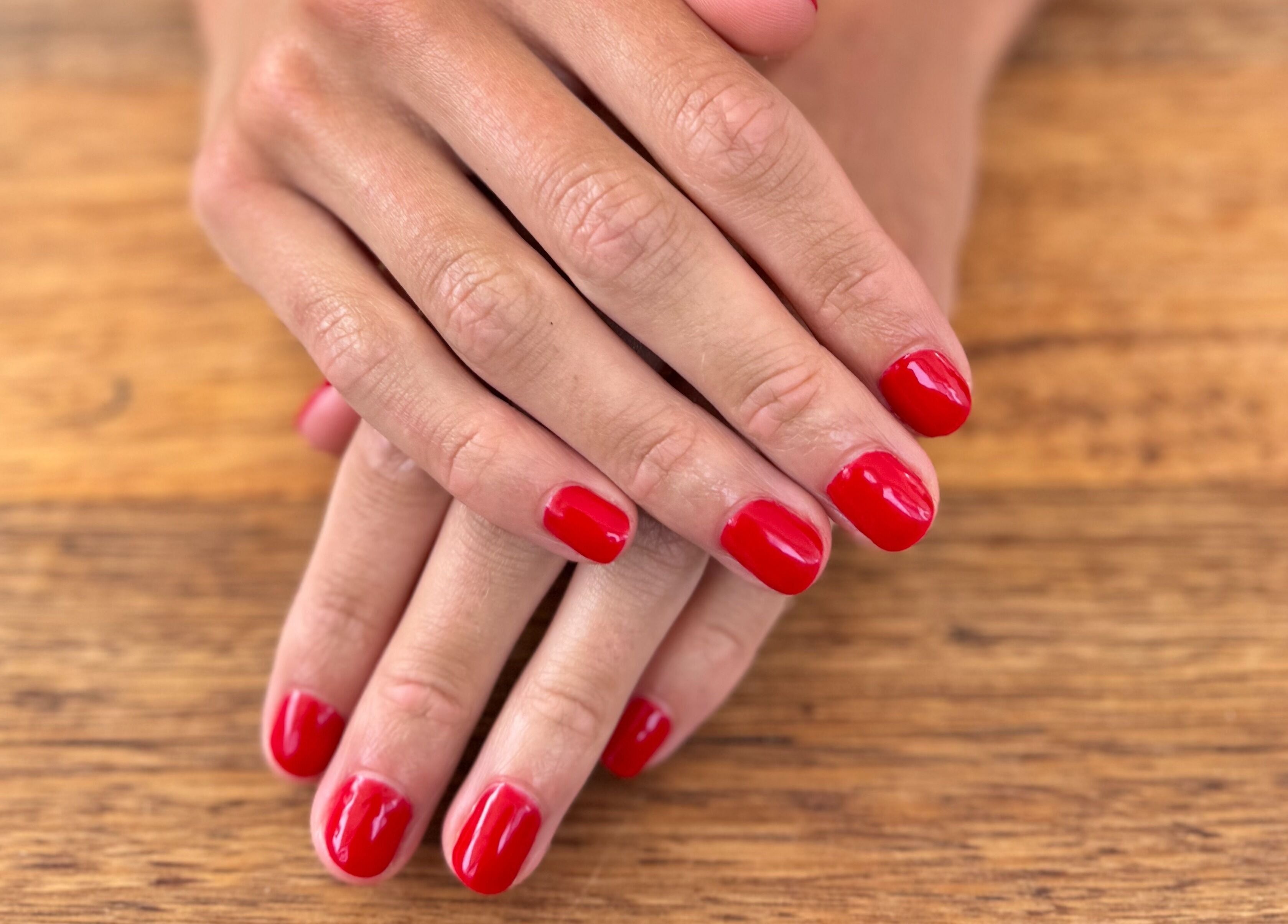 Elegant red nails manicure at Studio Rebecca Greaves, Devonport, Tasmania, AU on a wooden surface.