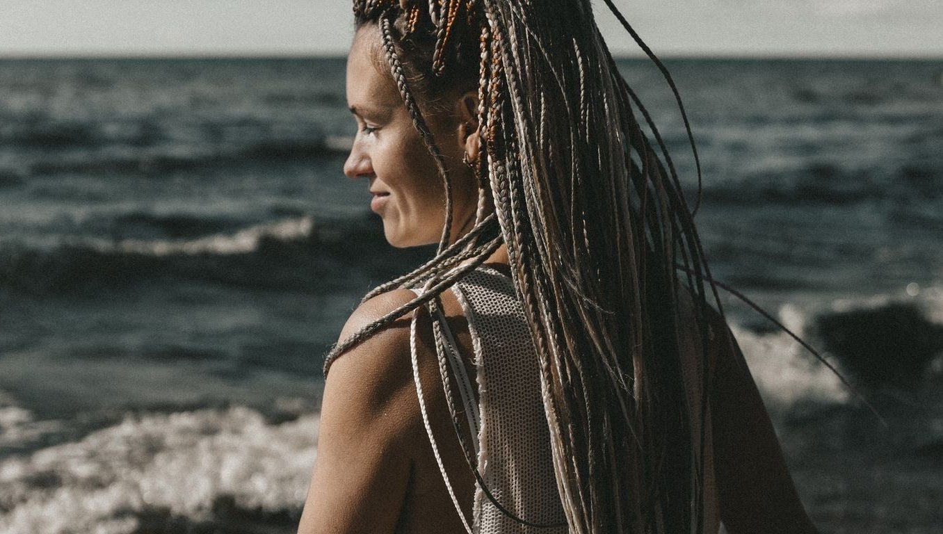 Woman with intricate braids from FOXY Braid House, Rīga, LV, gazing over a tranquil seaside view.