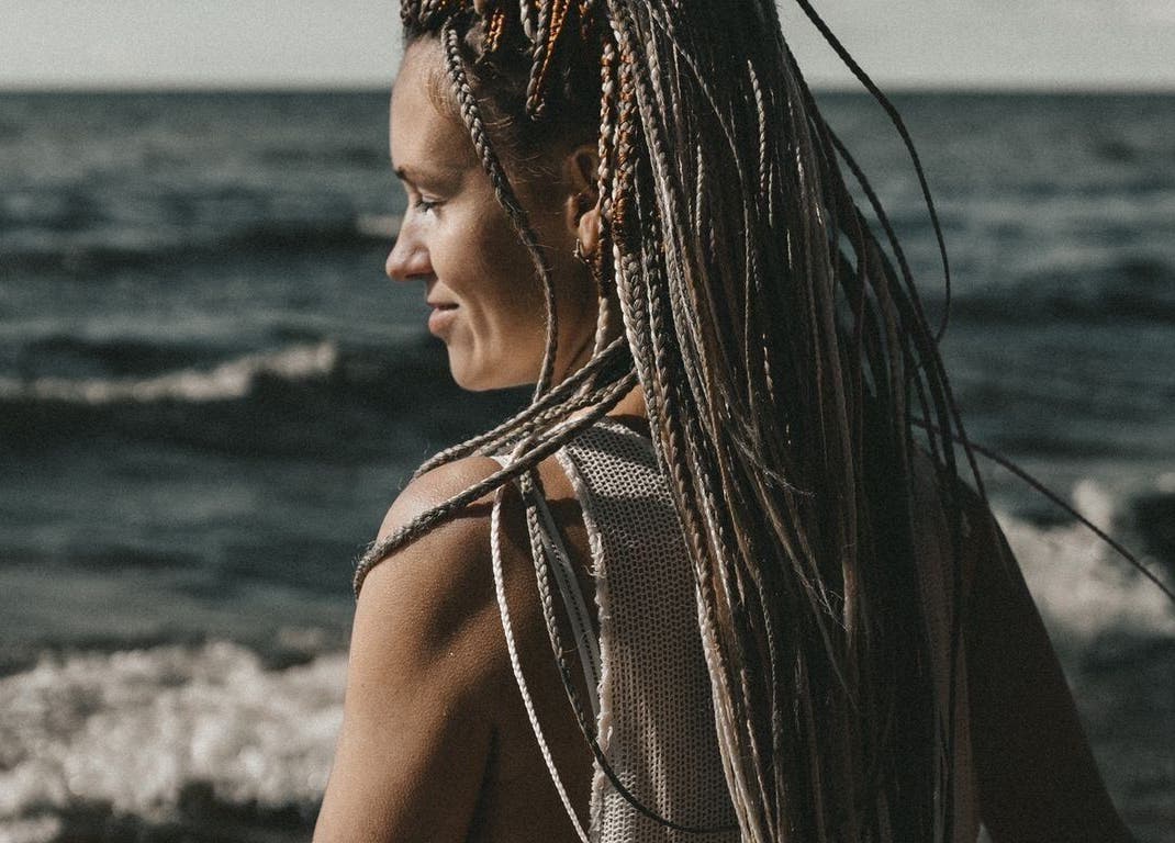 Woman with intricate braids from FOXY Braid House, Rīga, LV, gazing over a tranquil seaside view.
